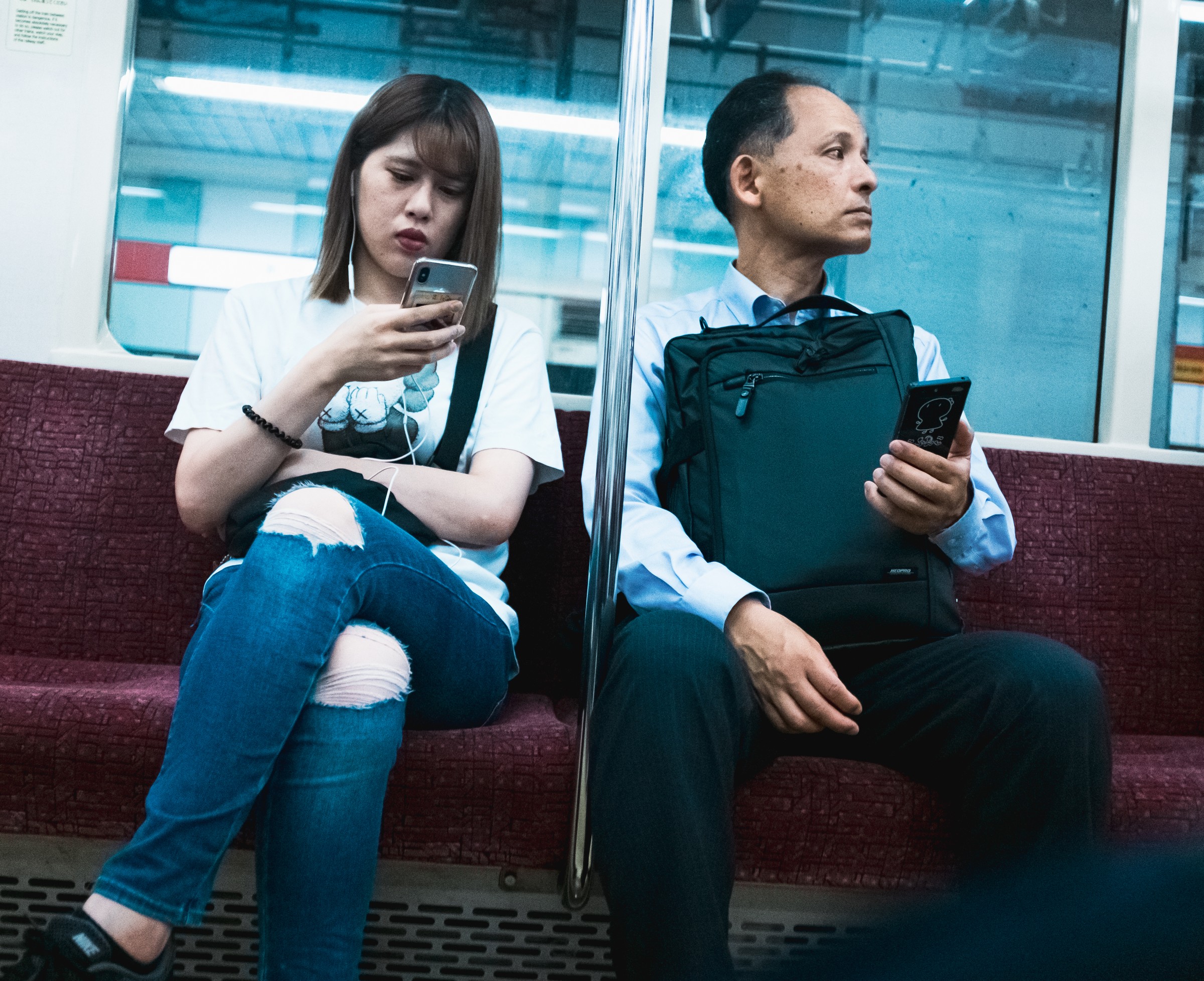 Two passengers sit back to back across a divider on a train.