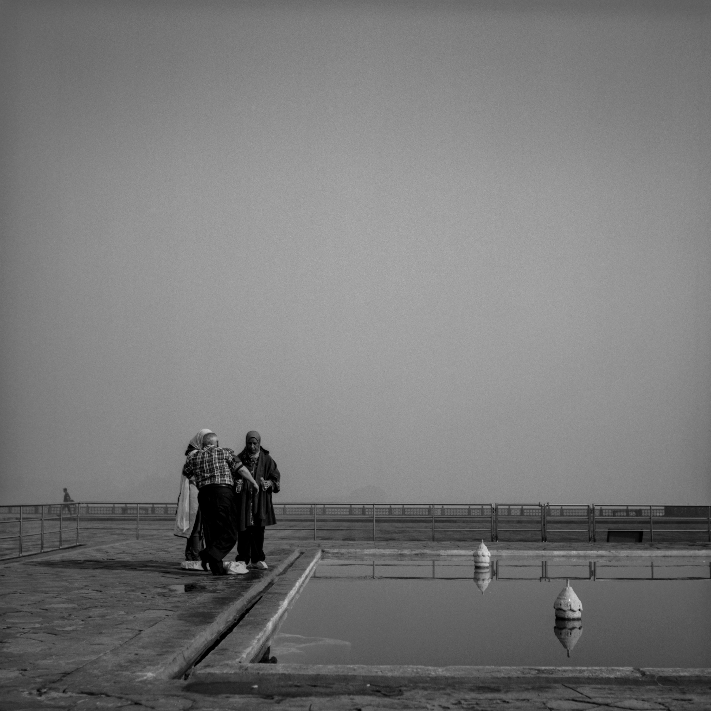 Visitors stand beside a reflecting pool beneath an open grey sky.