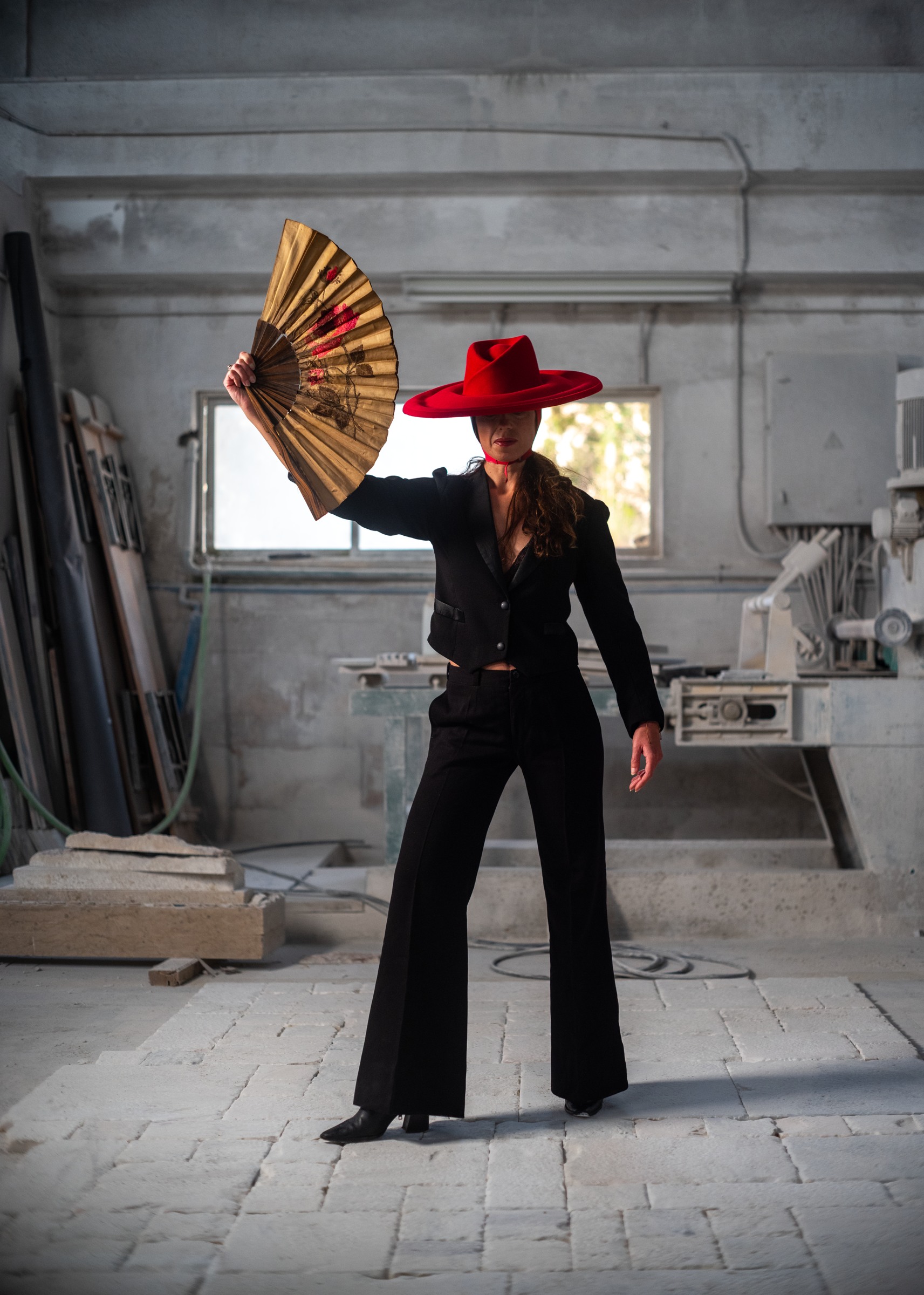Woman in a black suit and red hat holding an open fan